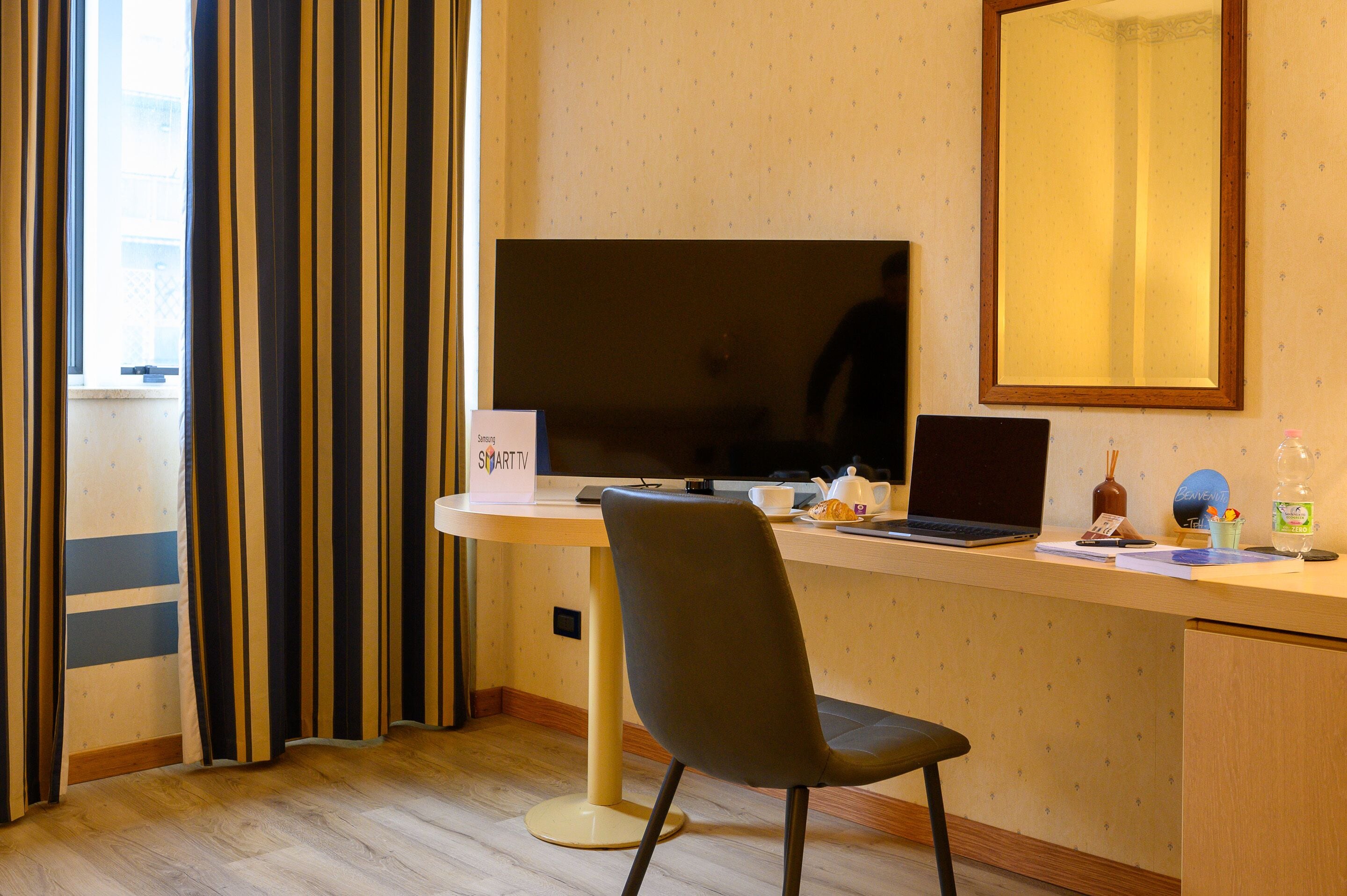 A hotel room with a desk, a laptop, a television, and a chair.