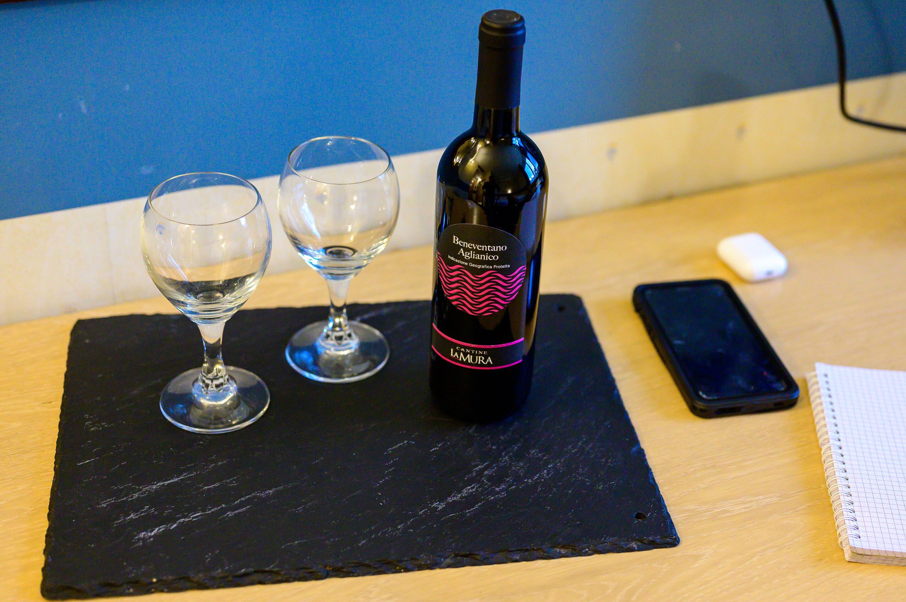 Une bouteille de vin, deux verres, un téléphone intelligent et un carnet sur une table.