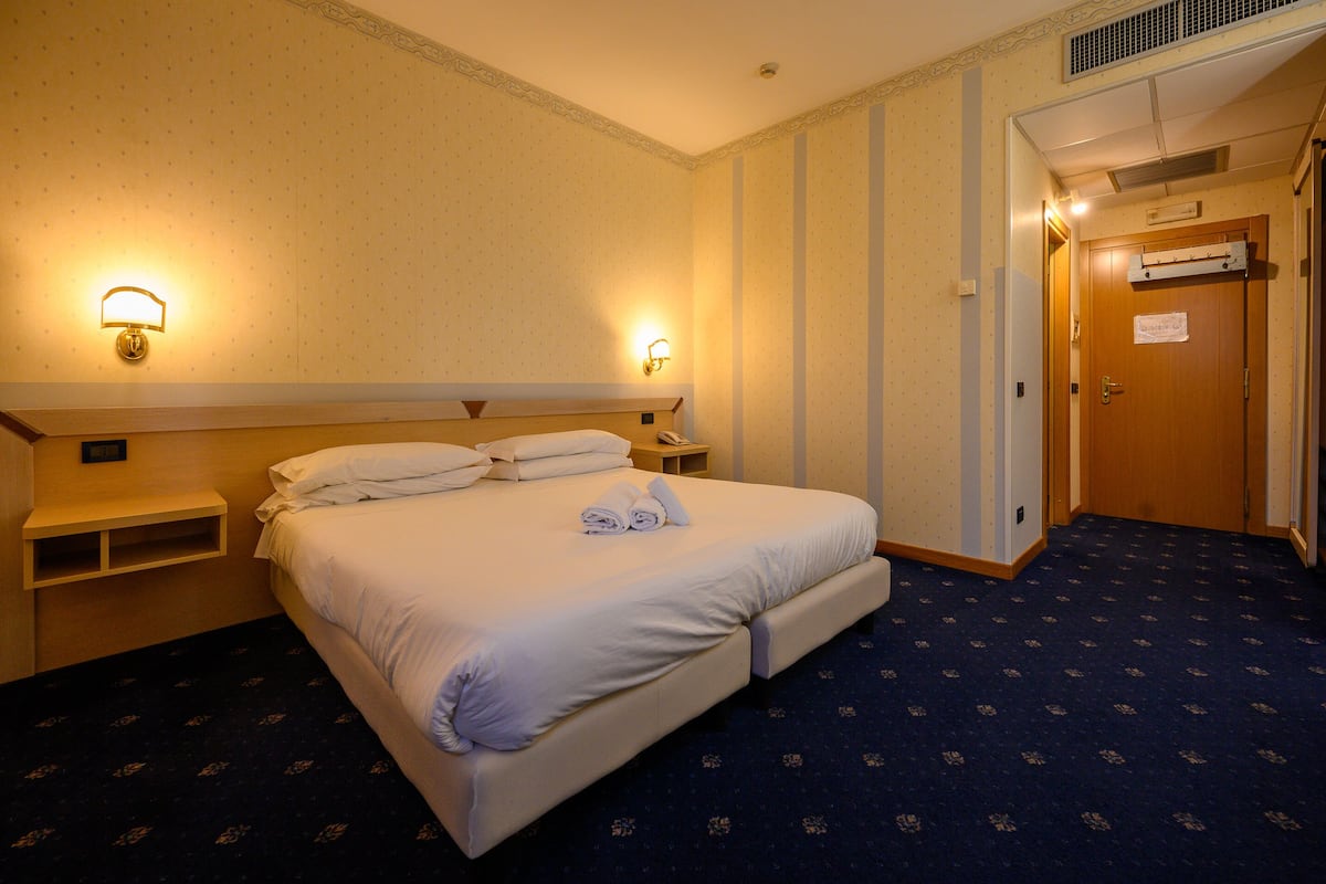 Ein Hotelzimmer mit einem großen Bett, zwei Nachttischlampen, einem Nachttisch und einer Tür mit einem Schild.
