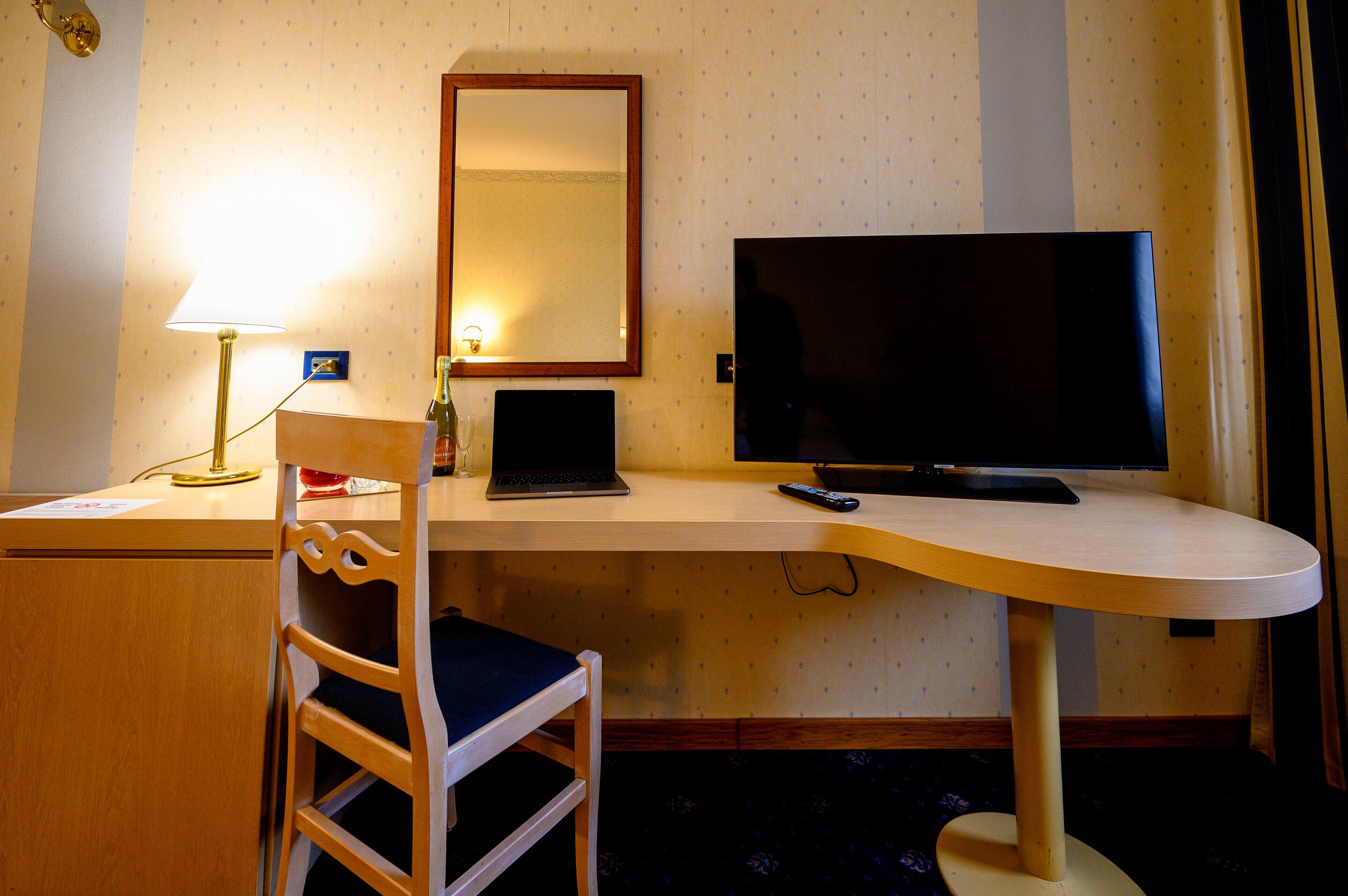 Una habitación de hotel con un escritorio, una silla, un televisor y una lámpara.