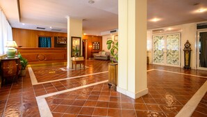 A spacious lobby with a wooden reception desk, a seating area with a sofa, and a large potted plant. - Hotel Torre di Pratolungo (Rome)