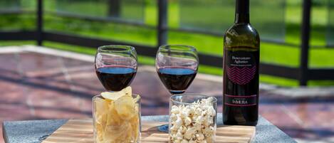 Une bouteille de vin, deux verres de vin rouge et des boîtes de chips et de pop-corn sur une planche en bois.