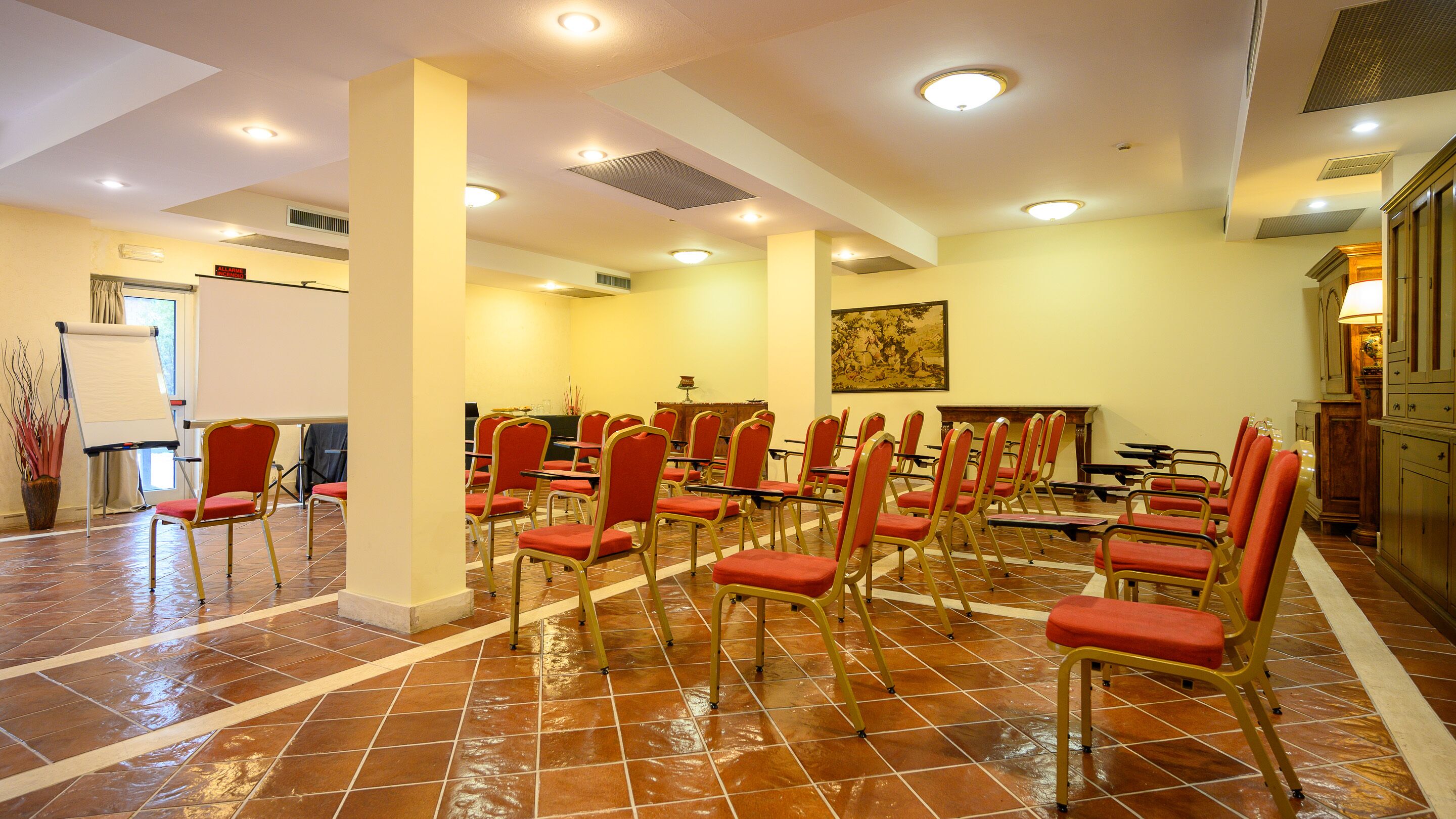 Un salón de conferencias con filas de sillas rojas, una pizarra y un cuadro en la pared.