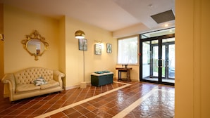 A spacious room with a large window, a sofa, a bench, and a mirror on the wall. - Hotel Torre di Pratolungo (Rome)