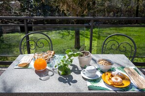 A table set outdoors with breakfast items including toast, juice, a plant, a bowl of cereal, a teapot, and a plate with pastries. - Hotel Torre di Pratolungo (Rome)