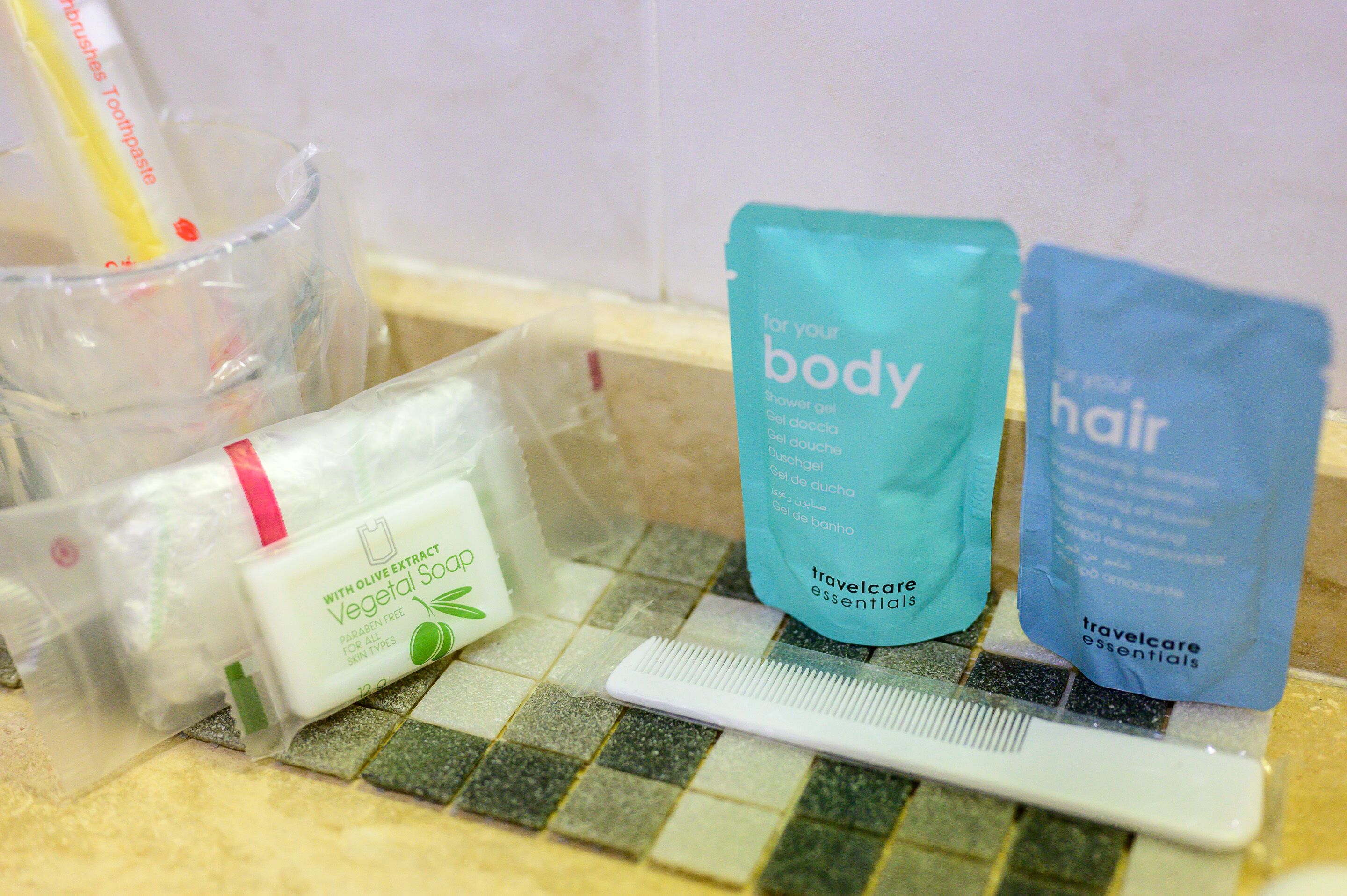 Toiletries including a shower gel, body wash, and hair care products on a tiled bathroom counter.