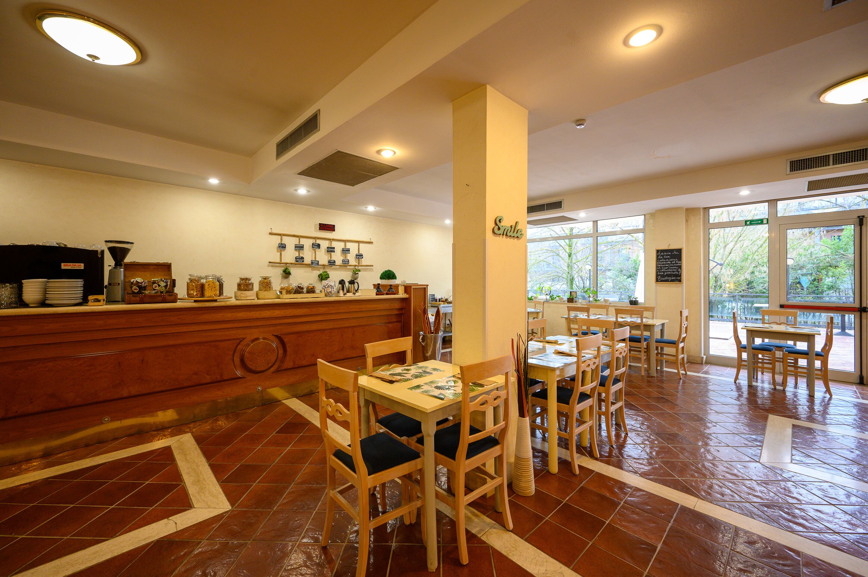 Un restaurante con mesas y sillas de madera, una barra con una máquina de café y vistas a zonas verdes al exterior.