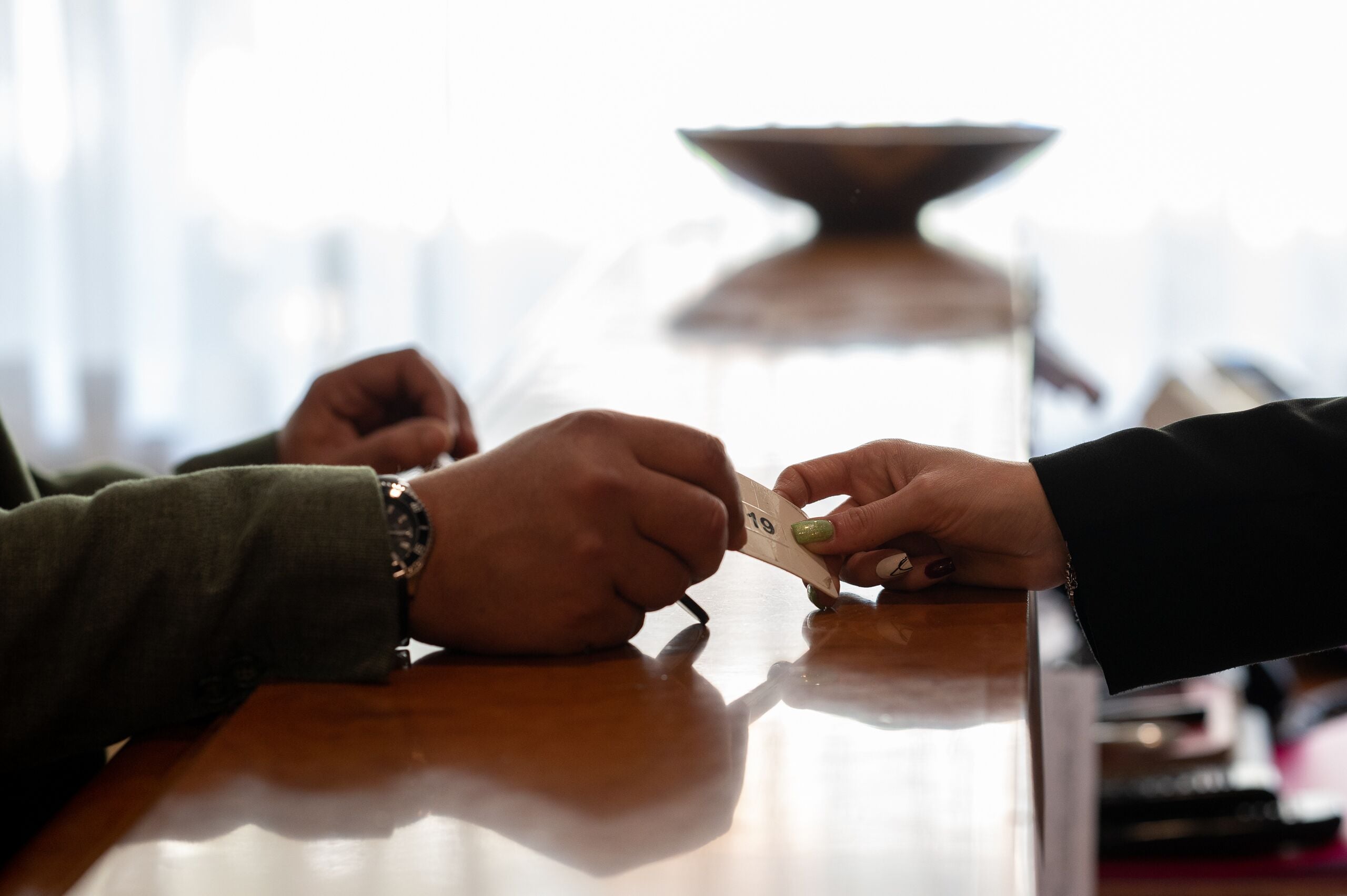 A close-up of hands exchanging a coin at a table with a reflective surface.