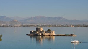 A historic fort on an island in a calm body of water with mountains in the background. - Nikolaos Pension (Nafplio)