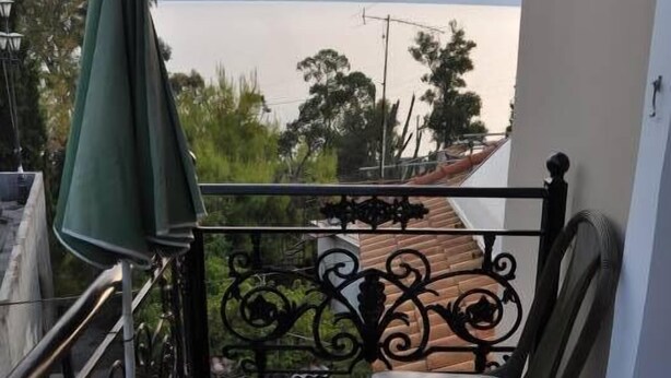 A balcony with a glass table and chair, overlooking a body of water and distant mountains. - Nikolaos Pension (Nafplio)