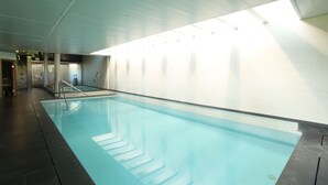 Une piscine intérieure à l’eau claire, dotée d’un sol carrelé et d’un plafond avec des spots encastrés.