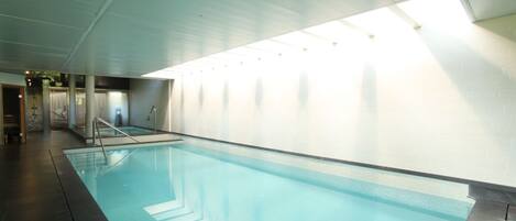 Una piscina interior con agua cristalina, suelo de baldosas e iluminación empotrada en el techo.