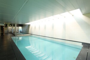 Una piscina interior con agua cristalina, suelo de baldosas e iluminación empotrada en el techo.
