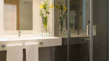 A modern bathroom with a glass shower enclosure, a large mirror, and a white sink with two towels.