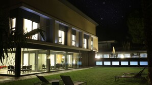 Un bâtiment moderne doté de grandes fenêtres, d’une pelouse verdoyante et d’un espace extérieur aménagé pour s’asseoir.