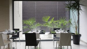 Un espace repas moderne avec un mur en briques, de grandes fenêtres et des plantes en pot.