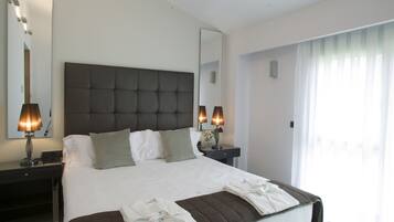 Una habitación de hotel moderna con una cama grande, dos lámparas de noche, un espejo y una ventana con cortinas traslúcidas.