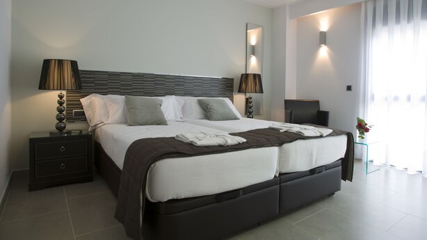 Une chambre d’hôtel moderne avec un grand lit, des lampes de chevet, une table de chevet, un miroir et une fenêtre avec des rideaux.