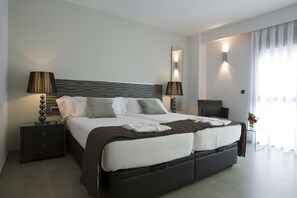 A modern hotel room with a large bed, bedside lamps, a nightstand, a mirror, and a window with curtains.