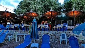 Un espace extérieur aménagé avec des murs en pierre, des chaises bleues et des parasols pour créer de l’ombre.
