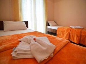 Une chambre d’hôtel avec deux lits, l’un recouvert d’une couverture orange et l’autre d’une couverture blanche. Une serviette blanche est posée sur la couverture.