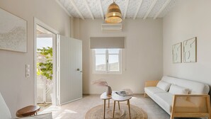 Una sala de estar con un sofá blanco, una silla de mimbre, un tapete redondo y una lámpara colgante.