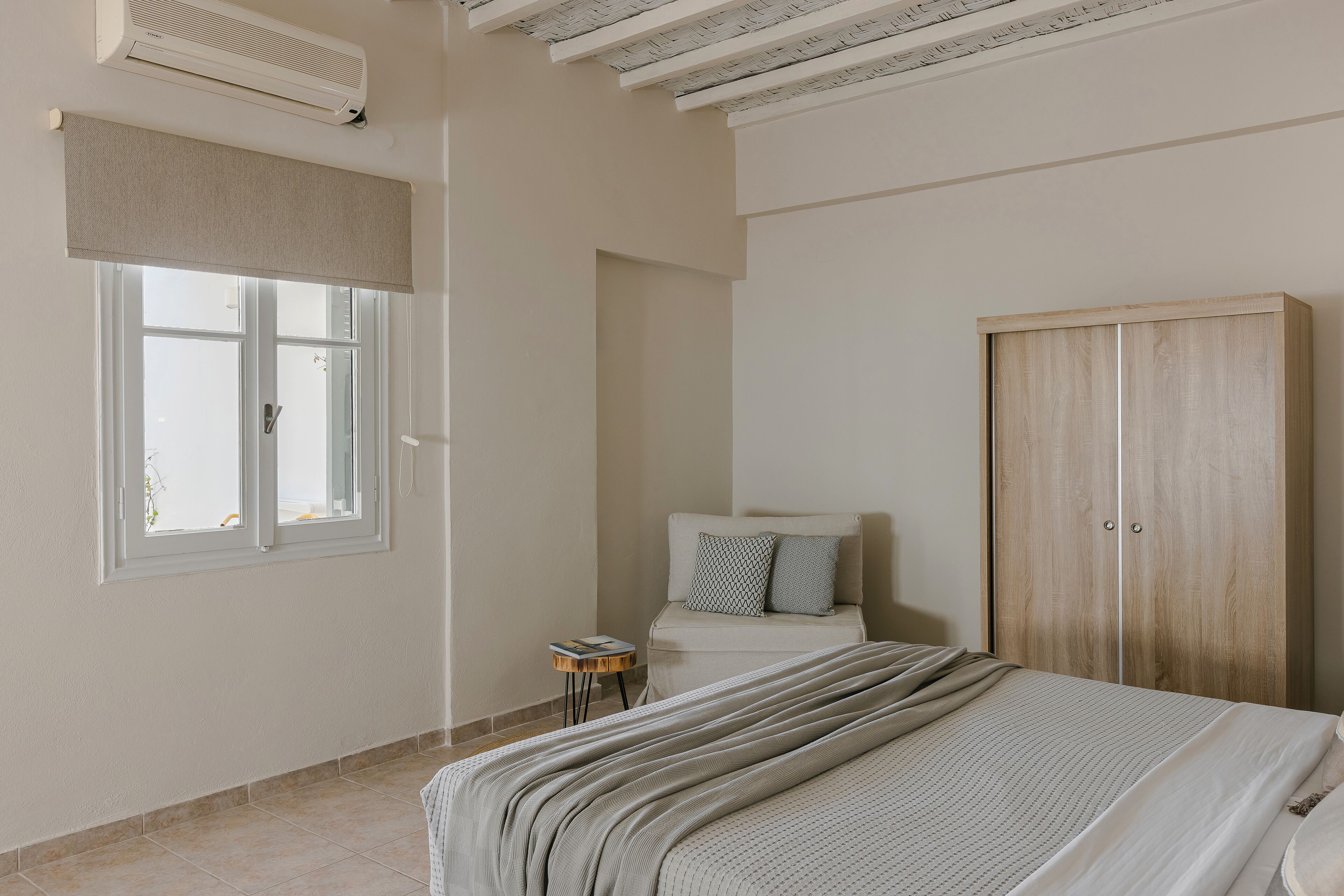 Un dormitorio con cama, armario, ventana con persiana y una mesita de noche.