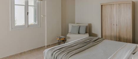 Un dormitorio con cama, armario, ventana con persiana y una mesita de noche.