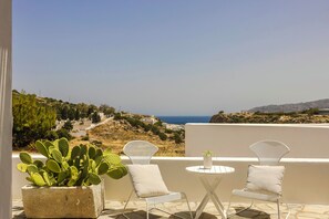 A terrace with two white chairs and a table, overlooking a coastal landscape with buildings and a clear sky. - Milaki Kimolos (Kimolos)
