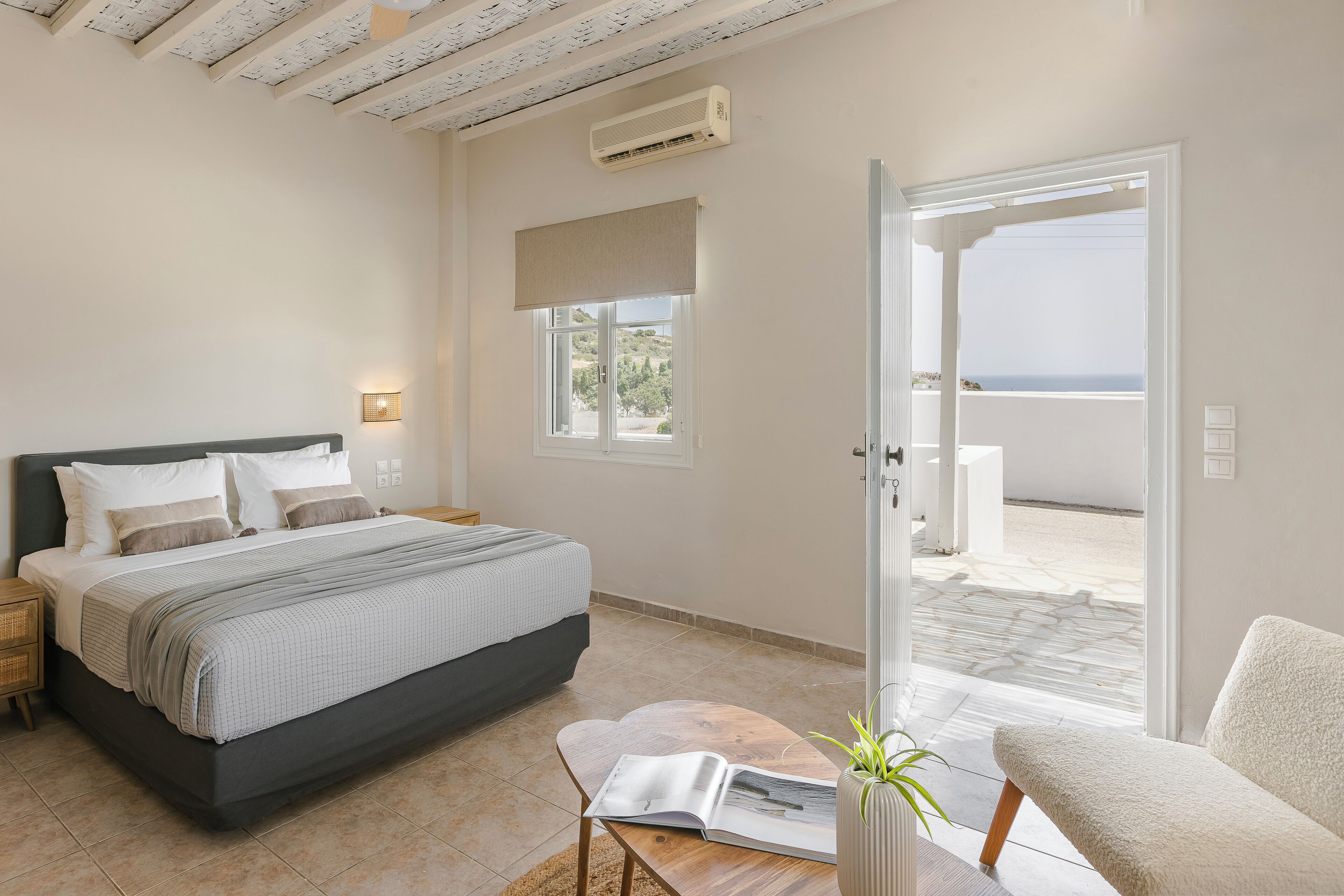 Un dormitorio con cama, mesitas de noche, una ventana con vistas y una puerta que da a un espacio exterior.
