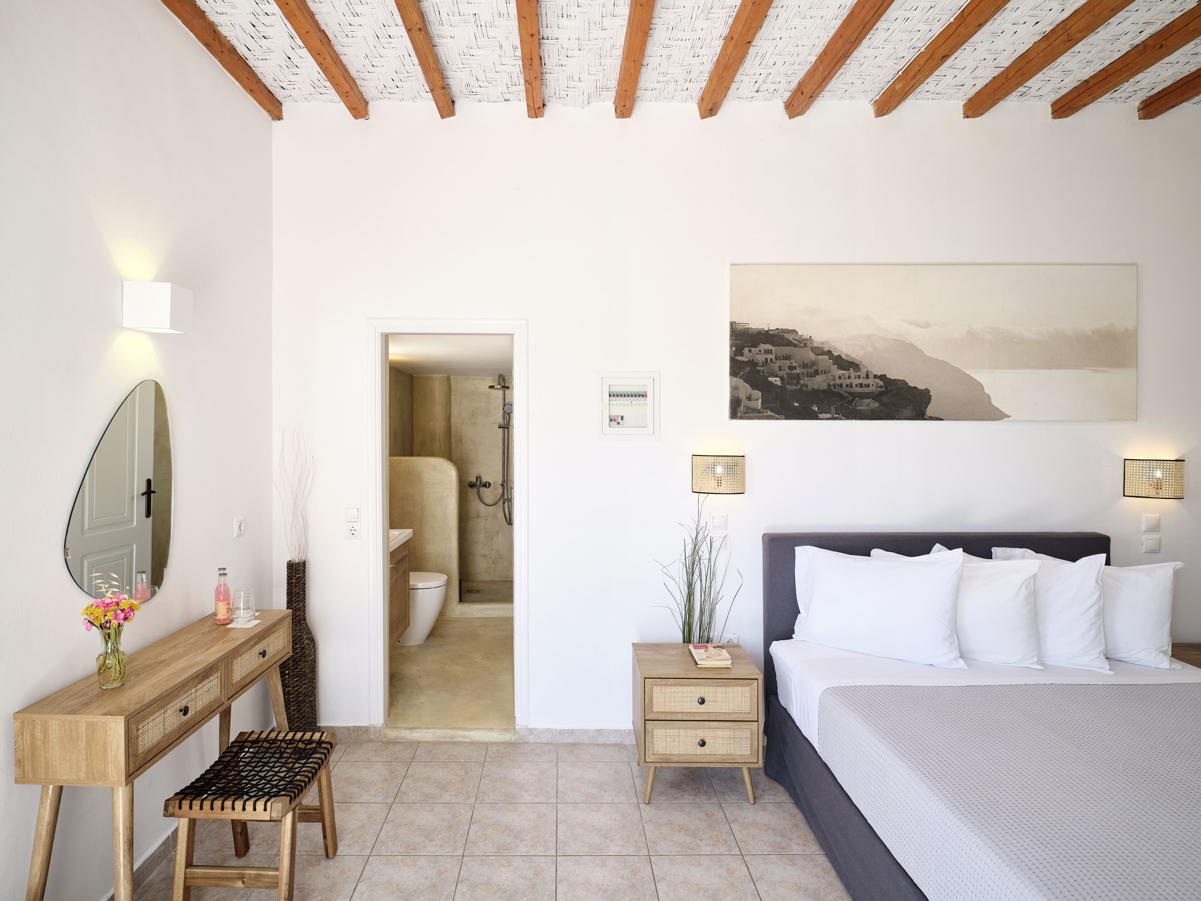 Een slaapkamer met een bed, nachtkastjes, een spiegel en een badkamer zichtbaar door een geopende deur.