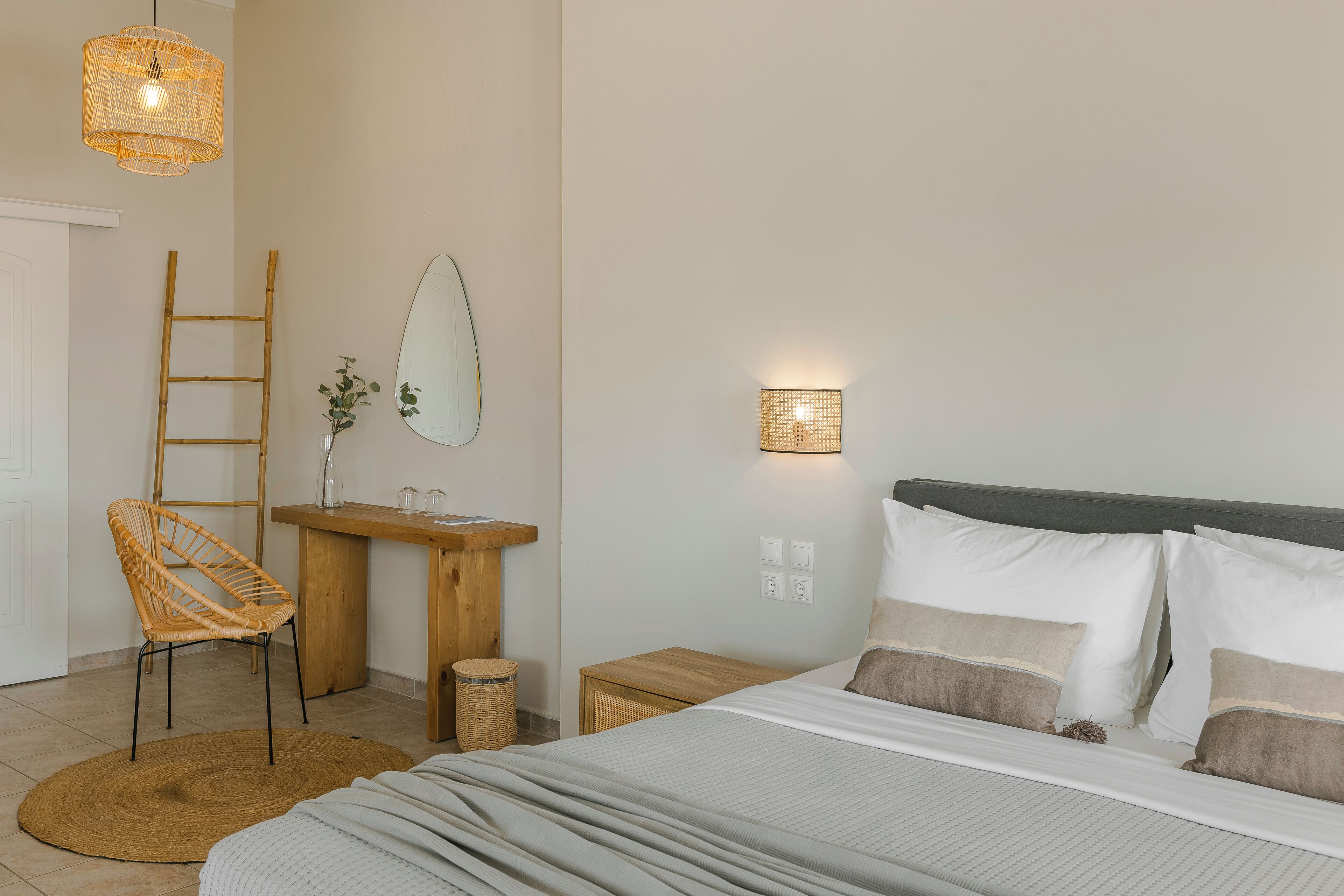 A bedroom with a bed, a wooden chair, a bedside table, a mirror, and a wall-mounted light fixture.