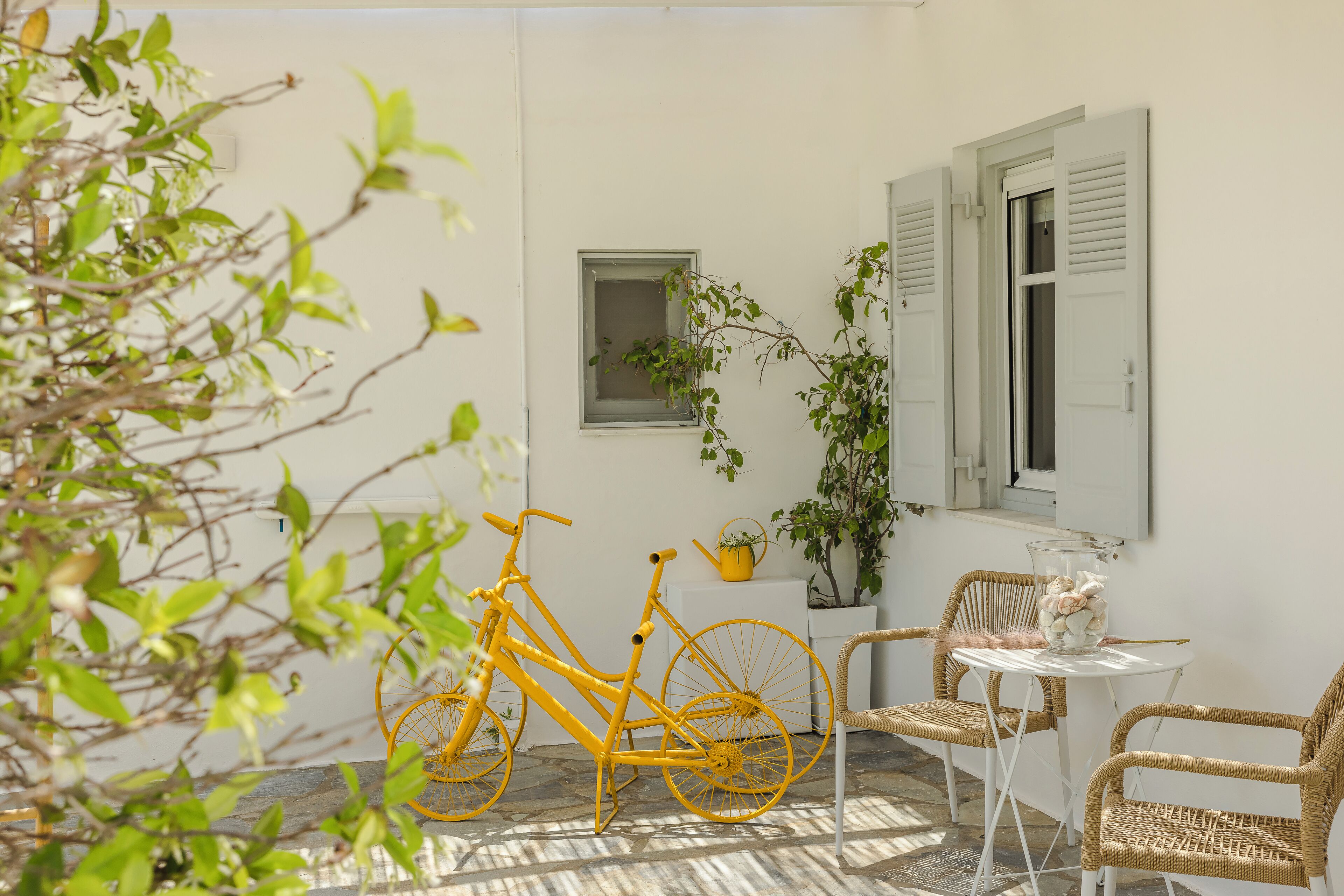 A patio with a yellow bicycle, wicker chairs, a small table, and potted plants.