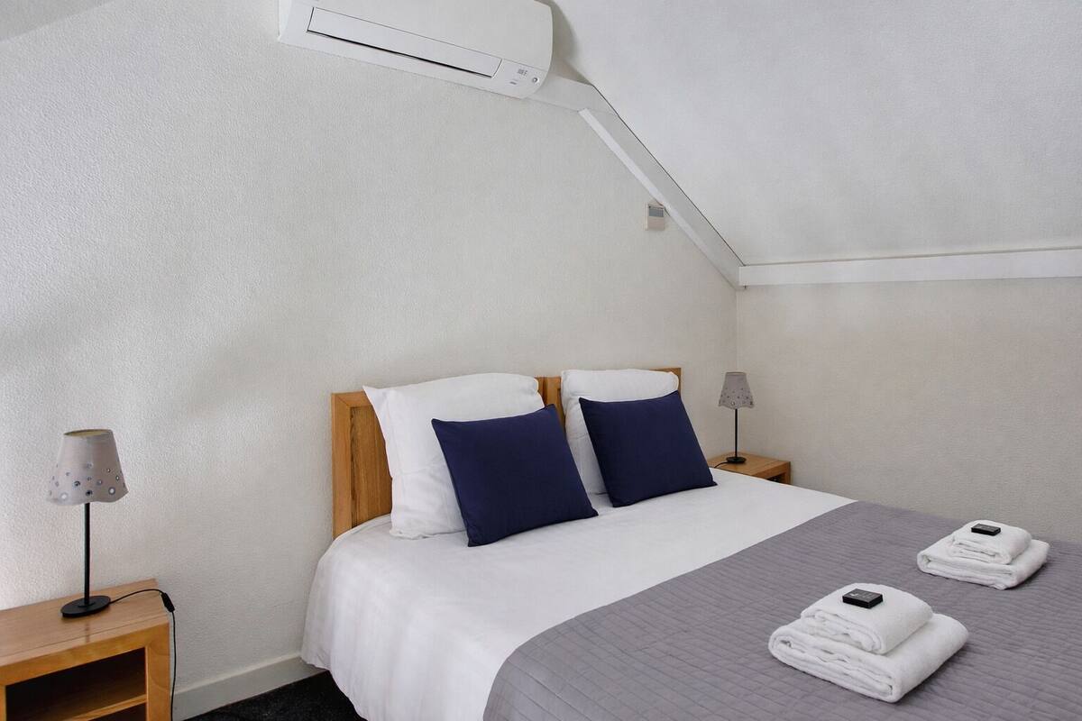 Ein Hotelzimmer mit einem Bett, zwei Nachttischen, einer Lampe und einem gefalteten Handtuch auf dem Bett.