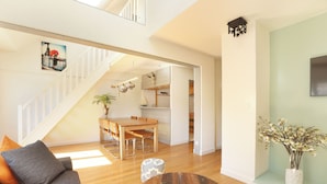A spacious living area with a wooden dining table, a sofa, and a coffee table. A staircase leads to an upper level. -  Les Lilas Serviced Apartments (Les Lilas)