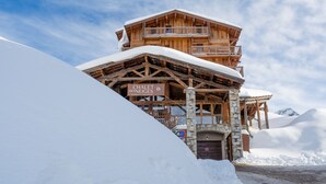 A wooden chalet with a stone base, snow-covered balconies, and a sign reading "Chalet des Neiges".