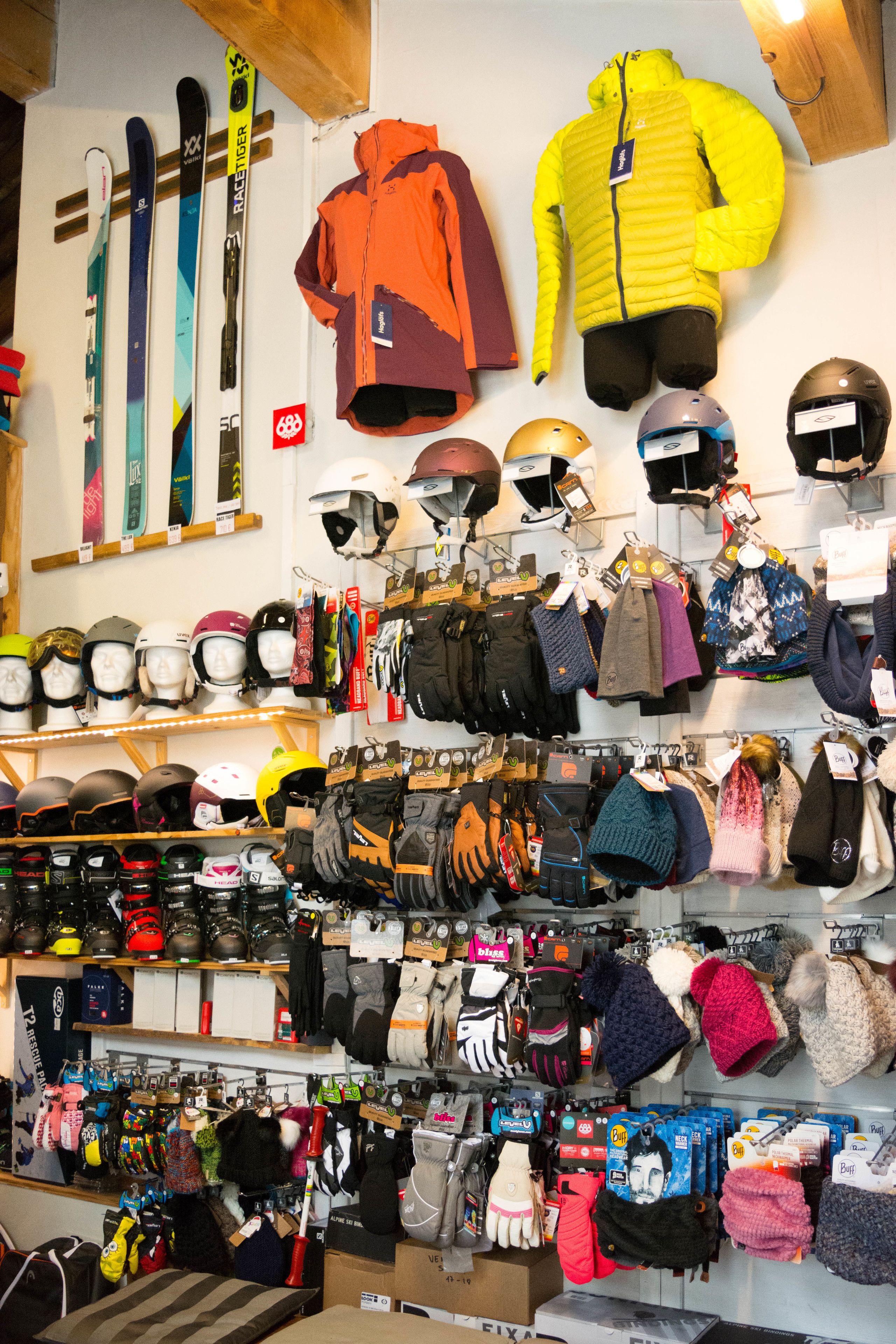 Een winkel met diverse wintersportartikelen en kleding, waaronder ski's, helmen en jassen.