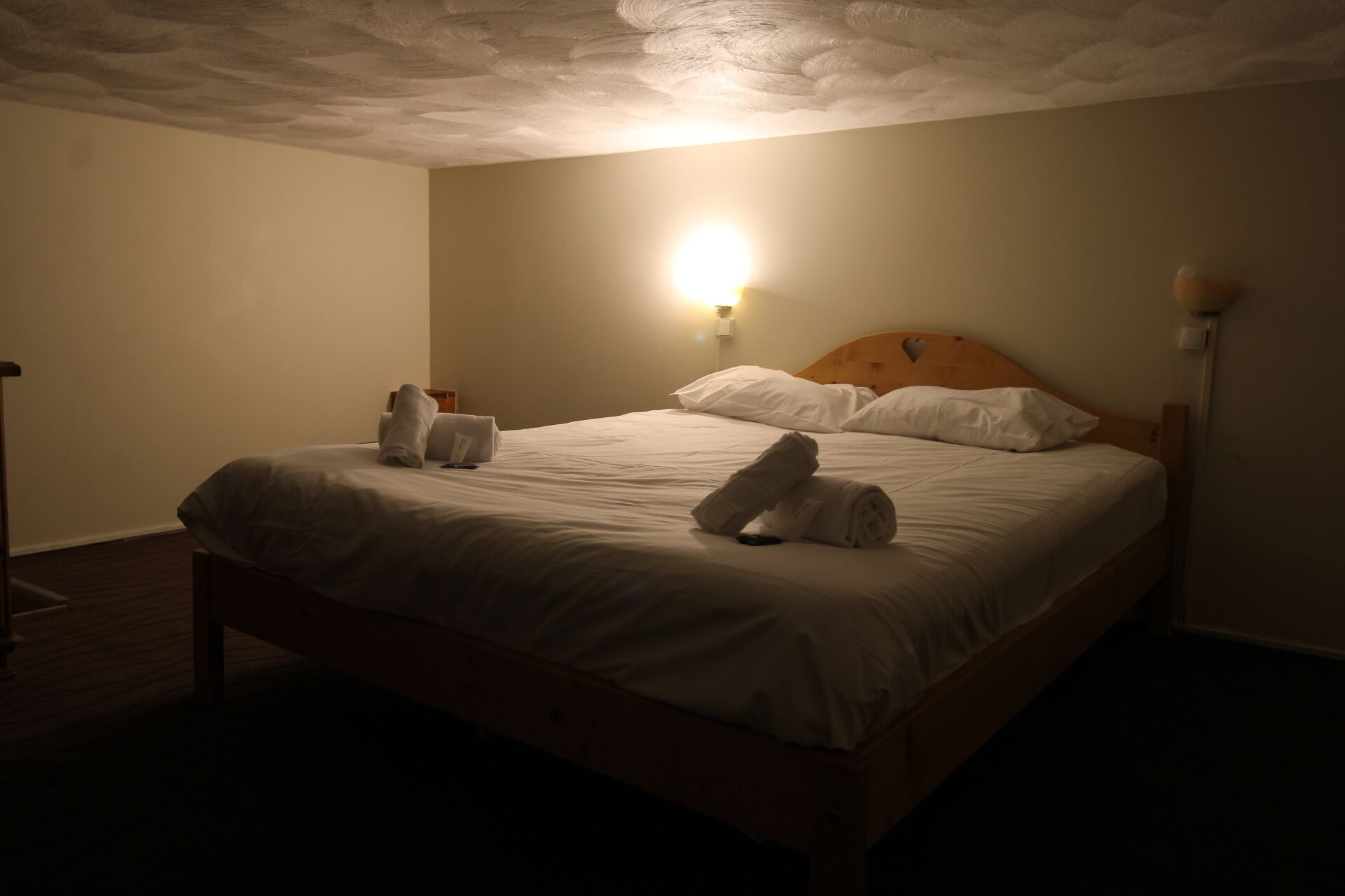 A hotel room with a wooden bed, white linens, and a wall-mounted light fixture.