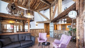 A rustic interior with a wooden ceiling, a black sofa, two pink armchairs, and a round table.