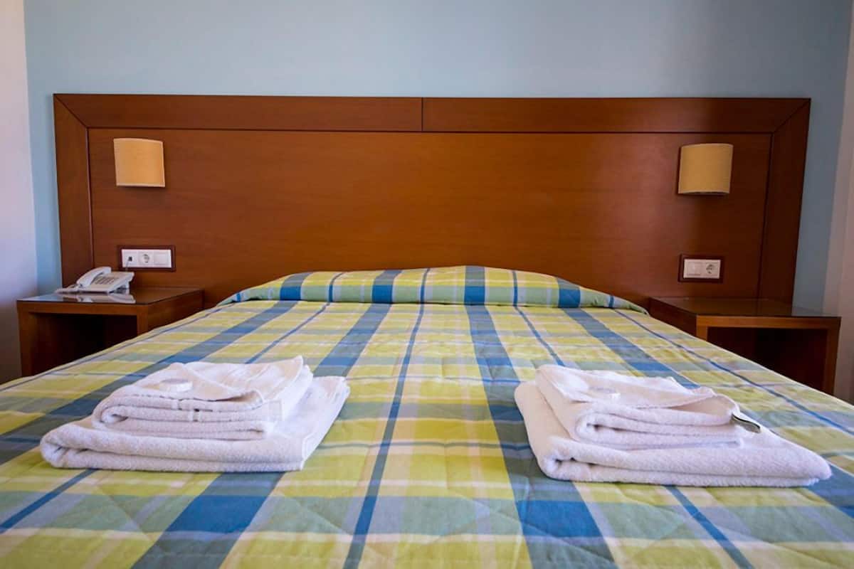 Quarto de hotel com uma cama grande, duas mesas de cabeceira, um telefone e duas toalhas dobradas na cama.