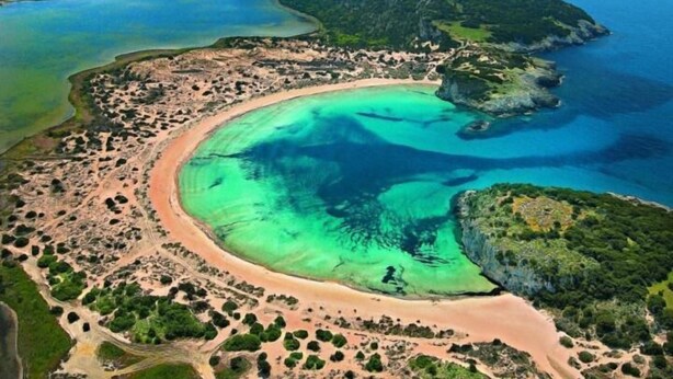 An aerial view of a coastal area with a curved bay, clear waters, and surrounding greenery. - Navarone (Pylos-Nestoras)