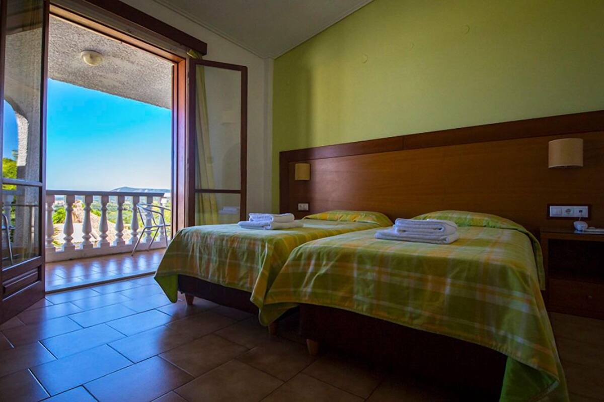 Quarto de hotel com duas camas, varanda e vista para o exterior.