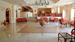 A spacious lobby with a high ceiling, a chandelier, and a central seating area with red upholstered chairs. A large vase is placed in the middle of the lobby. - Navarone (Pylos-Nestoras)