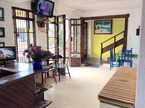 A reception area with a television, a desk, chairs, a staircase, and a painting on the wall. - La Posada de Lulu (San Andrés)