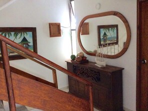 A wooden staircase with a railing, a wooden cabinet with decorative carvings, and a wall-mounted mirror reflecting a beach scene. - La Posada de Lulu (San Andrés)