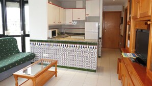 A compact living space with a kitchenette, a glass-top coffee table, and a television. - Apartamentos Surfing 3000 (Peniscola)