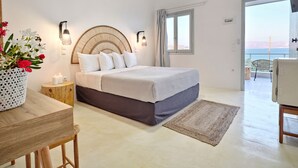 A bedroom with a bed, bedside table, lamp, and a view of the sea through a window.