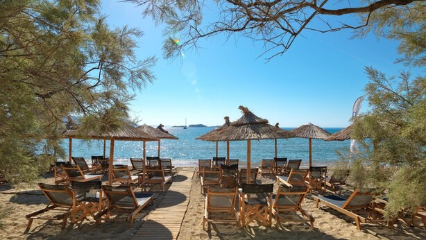 A beach with wooden deck chairs and thatched umbrellas, overlooking a calm sea.