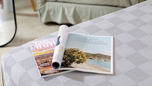 A bed with a magazine on it, a chair, and a ladder in a room.