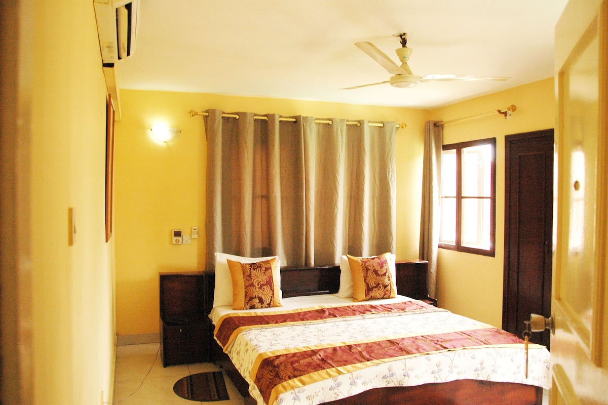 A bedroom with a bed, curtains, a ceiling fan, and a door.